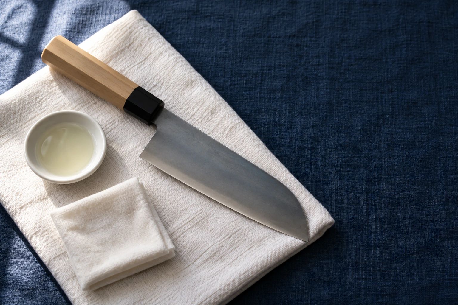 Ein abgetrocknetes Santoku aus Kohlenstoffstahl auf weißem Handtuch, mit Kamelienöl und einem weichen Tuch