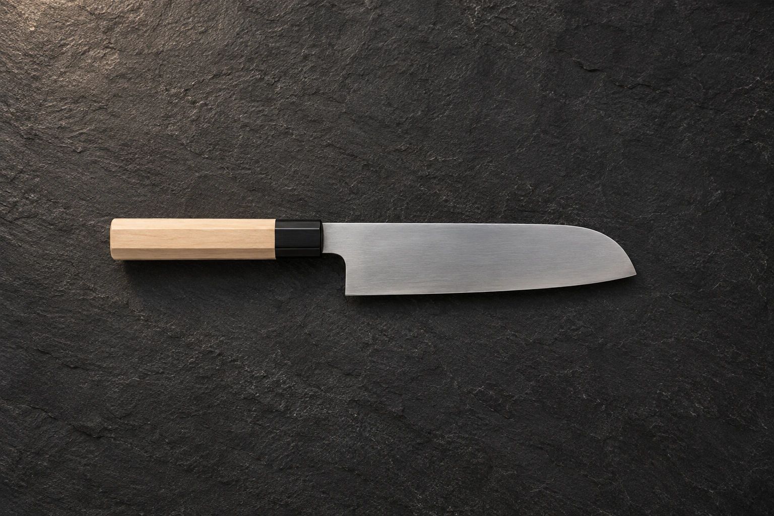 A santoku with a wooden handle on dark slate, seen from above