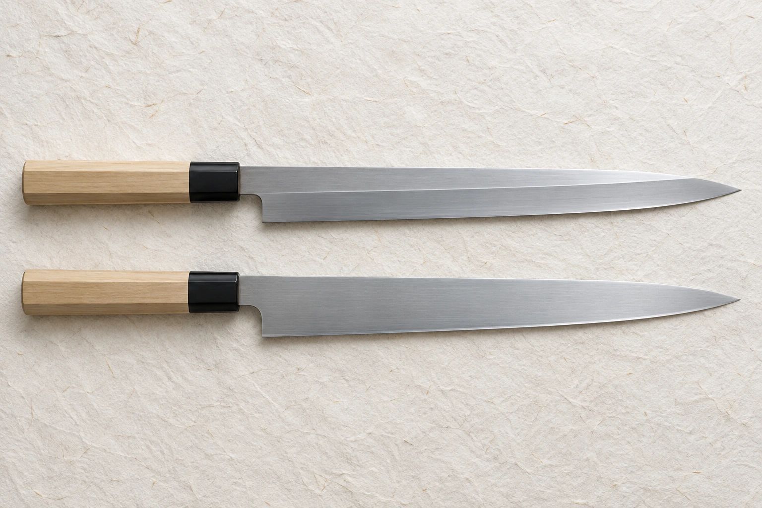 A single-bevel yanagiba with a visible shinogi line above a double-bevel sujihiki of the same length, on washi paper