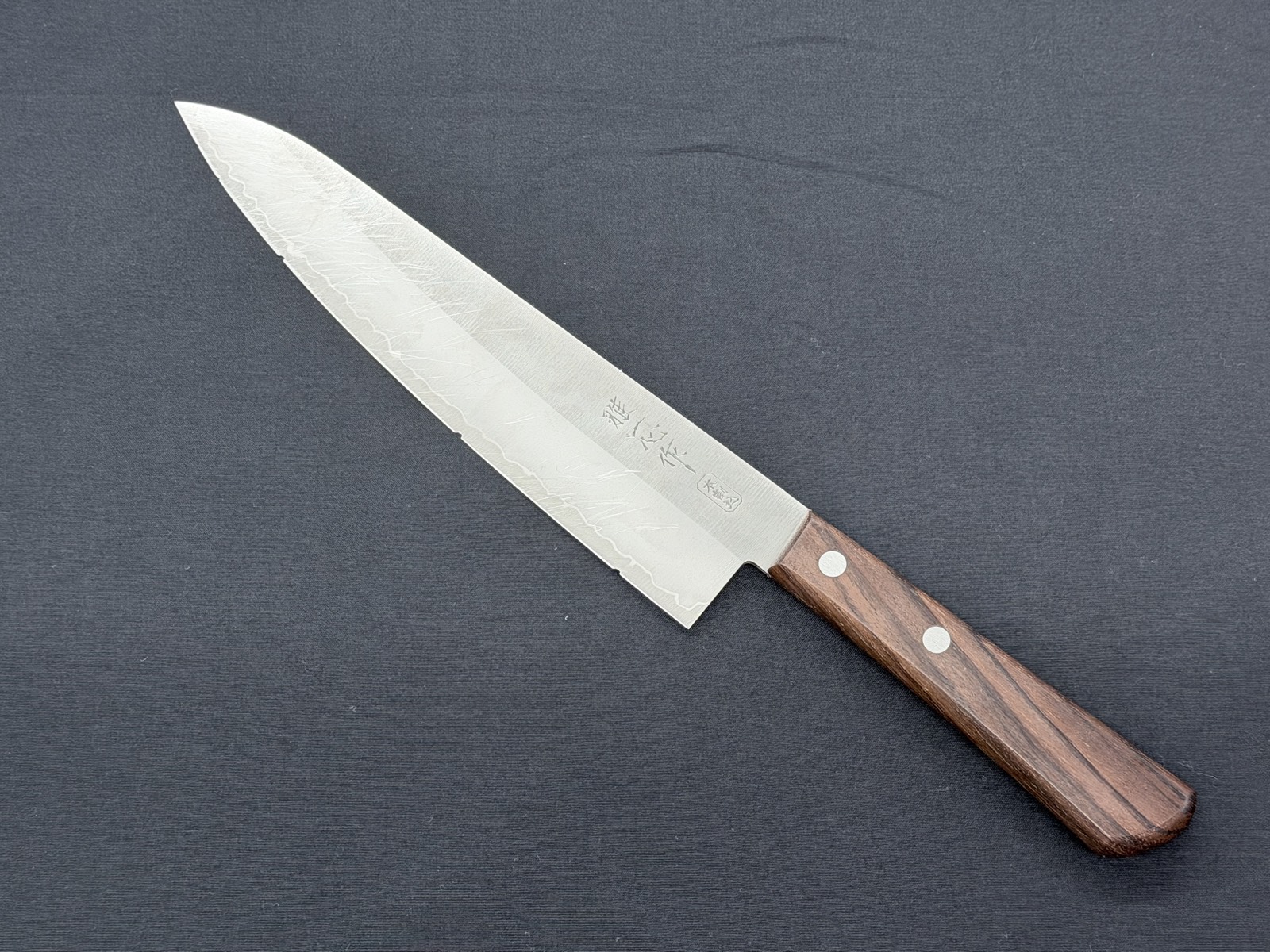 Six identical santoku knives lined up, each dulled on the edge and blade face under the same conditions before being sent out for sharpening