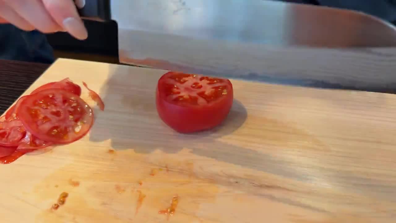A tomato being sliced on a wooden board during our Kappabashi santoku test